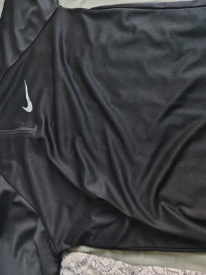 Svart långärmad träningströja Nike - Säljer en svart långärmad träningströja från Nike med vit logga på bröstet. Tillverkad i ett lätt och snabbtorkande funktionsmaterial som passar perfekt till träning eller löpning. Tröjan har en enkel och sportig design. Den passar mest som M