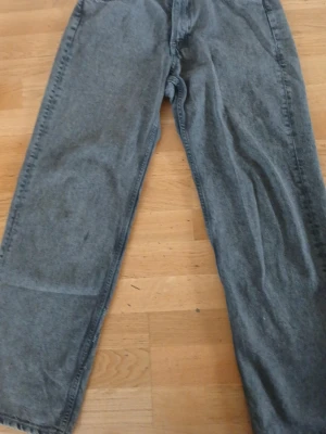 Gråa raka jeans - Säljer ett par gråa jeans med rak passform och klassisk femficksdesign. Jeansen har en avslappnad look och är tillverkade i denim. Perfekta för dig som gillar en enkel och stilren stil.
