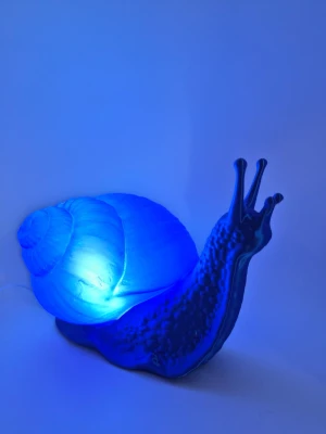 Blå nattlampa  - Unik blå lampa formad som en snigel, tillverkad i plast. Lampan lyser upp med ett mjukt blått sken och har detaljerad struktur på skal och kropp. Perfekt som dekoration eller mysbelysning i rummet. Ljuskälla ingår ej, funkar lika fin med ledvärmeljus eller ledpuck. 