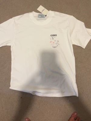 Vit t-shirt med tryck från Casa - Vit t-shirt från Casa med färgglatt sportigt Klassisk passform med rund hals och korta ärmar. Perfekt för dig som gillar en clean look med en twist.pris kan diskuteras