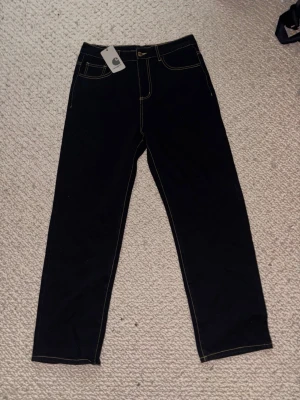 Svarta raka jeans från Carhartt - Snygga svarta jeans från Carhartt med raka ben och kontrastsömmar. Klassisk femficksmodell med Carhartt-logga på bakfickan. Jeansen har en enkel och clean look som passar till det mesta. 