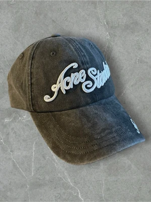Grå keps från Acne Studios - Snygg grå keps från Acne Studios med broderad logga i vitt framtill. Klassisk böjd skärm och justerbar rem bak. Tillverkad i 100% bomull för en bekväm och avslappnad look. Perfekt accessoar för att lyfta din outfit.