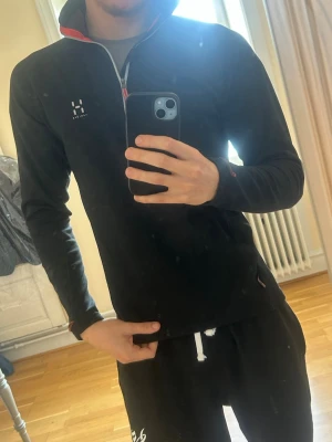 ”Vintage” Haglöfs fleece  - Tjena säljer en gammal Haglöfs fleece med halv dragkedja och hög krage. Diskreta röda detaljer vid dragkedjan och insidan av kragen. Långärmad modell med tumhål vid ärmsluten, perfekt för lager-på-lager och outdoor.