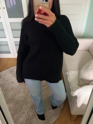 Svart ribbstickad oversized tröja - Mysig svart stickad tröja med ribbad struktur och avslappnad, oversized passform. Tröjan har långa ärmar och rund halsringning. Perfekt att bära till jeans eller leggings för en chill look.