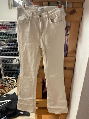 Beiga bootcut jeans från Only - Snygga beiga jeans från Only med bootcut-modell och klassisk femficksdesign. Jeansen har normal midja och är tillverkade i ett mjukt denimtyg med lite stretch för extra komfort. Perfekta för dig som vill ha en clean och stilren look.