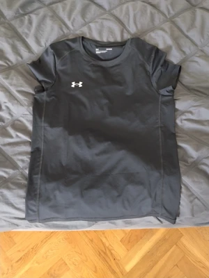 Svart träningströja från Under Armour - Svart kortärmad träningströja från Under Armour med vit logga på bröstet och ryggen. Tillverkad i ett lätt och stretchigt funktionsmaterial som andas, perfekt för intensiva träningspass och sportaktiviteter.