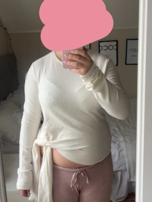 Vit långärmad topp med knyt - Säljer en vit långärmad topp med rund hals och snygg knytdetalj i sidan. Toppen har en enkel och clean look som passar till mycket. Materialet känns mjukt och stretchigt. Aldrig använd och säljer eftersom den ej satt som jag trodde