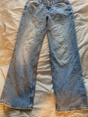 Ljusblåa raka jeans med rå kant - Säljer ett par ljusblå jeans med en rak form som går in lite mer mot fotlederna. Dem har en fransig, rå kant längst ner. Jeansen har klassiska fem fickor och bälteshällor. Materialet är denim och de har en avslappnad vintage vibe.