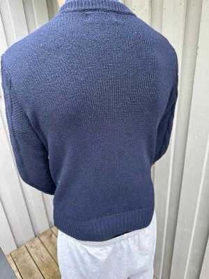 Mörkblå kabelstickad tröja - Säljer en mörkblå kabelstickad tröja med rund hals och ribbade muddar. Tröjan har ett klassiskt flätmönster framtill och är gjord i ett mjukt, tjockt material som håller dig varm. Perfekt för dig som gillar stilrena och tidlösa plagg.