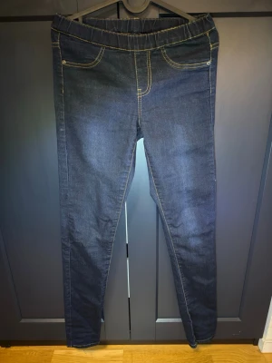 Mörkblå jeansleggings med resår - Snygga mörkblå jeansleggings med resår i midjan och kontrastsömmar. De har fejkade framfickor och riktiga bakfickor. Tight passform och stretchigt material som ger en bekväm känsla. Perfekta till en avslappnad look.