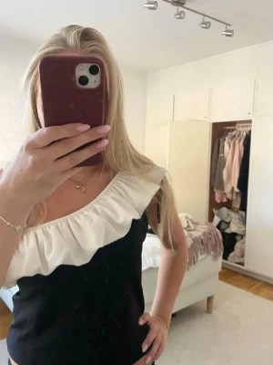 Svart offshoulder topp med volang - Snygg svart topp med bred vit volang längs offshoulder-kragen. Toppen är ärmlös och har en croppad passform som ger en trendig look. Perfekt för dig som vill sticka ut med en unik detalj på din outfit💓passar mig som vanligtvis har S💓