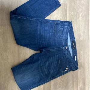 Blå Replay Anbass jeans, stl 31 - Snygga blå jeans från Replay, modell Anbass. Klassisk femficksdesign med Replay-logga på bakfickan och läderpatch i midjan. Jeansen har en rak passform och är tillverkade i mjukt denimtyg som sitter skönt hela dagen. Längden är anbassad till strl 31