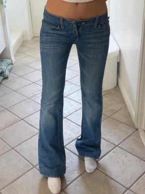 Hollister low waist jeans - Storlek xxs/xs. Rakt över midjemått 34cm. Innebenslängd 77cm. ett par klassiska blå bootcut jeans med låg midja och lätt slitna detaljer. Jeansen har fem fickor och stängs med knapp och dragkedja.