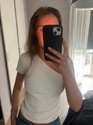 Vit ribbad oneshoulder topp - Säljer en vit ribbad topp med oneshoulder-design och kort ärm. Toppen är figurnära, 