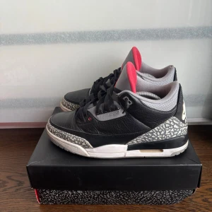 Nike Air Jordan 3 Black Cement - Klassiska Nike Air Jordan 3 Black Cement sneakers med svart och grått läder, ikoniskt elefantmönster på tå och häl samt röda detaljer på insidan. Tjock vit sula med synlig Air-enhet och tydlig Nike Air-logga på hälen. Perfekta för dig som gillar streetwear.Skick kan ses på bilderna