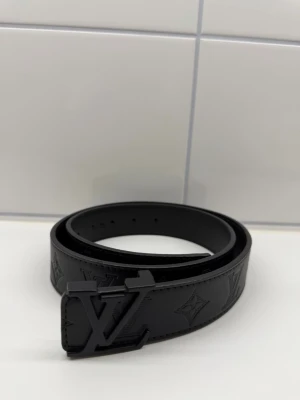 L V bälte  - Snyggt svart klassiskt skärp i skinn med svart spänne. Perfekt accessoar för att lyfta vilken outfit som helst med en exklusiv touch.
