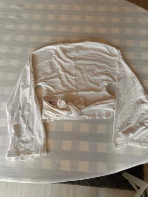Vit topp med knyt - Säljer en vit topp med långa ärmar och knyt i ryggen. Toppen har en enkel och clean design, perfekt att styla med jeans eller kjol. Tillverkad i mjukt bomullsmaterial för en skön känsla.