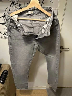 Grå raka jeans från Jack & Jones - Oanvända, Snygga grå jeans från Jack & Jones med rak passform och klassisk femficksdesign. Jeansen har en ljusgrå tvätt och är tillverkade i bomull med en liten stretch för extra komfort. Perfekta för en avslappnad och trendig look.
