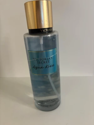 Victoria's Secret Aqua Kiss mist - Fräsch body mist från Victoria's Secret i doften Aqua Kiss. Flaskan är genomskinlig med blå etikett och har ett elegant guldigt lock. Hela flaskan är 250 ml men den har dock använts, finns ca 40% kvar.