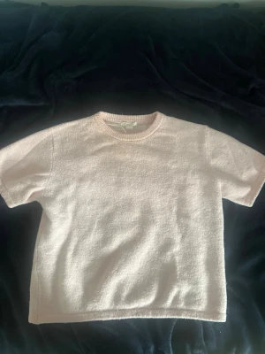 Ljusrosa topp från Gina Tricot - Supersöt ljusrosa topp från Gina Tricot med korta ärmar och rund hals. Materialet känns mjukt och lite fluffigt, perfekt för en chill och enkel look. Passar till allt från jeans till kjol och är enkel att styla.