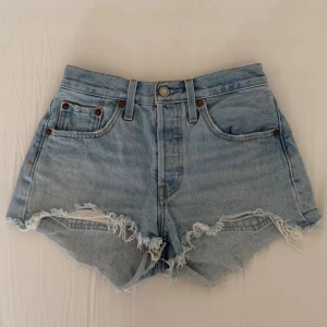 Levis shorts  - Säljer dessa Levis jeans 501 short. Medel till hög midja med lite fransiga kanter där nere. Super bra skick endast använda få tal gånger. Har legat vikta ett tag därav lite väck. Super snygga nu till sommaren. Storlek W25. PRIS KAN DISKUTERAS VID SNABBT KÖP