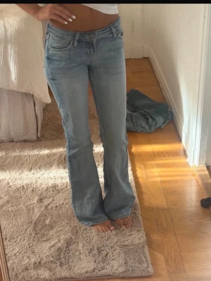 Ljusblå bootcut jeans - Säljer ett par ljusblå bootcut jeans med klassisk femficksdesign och normal midja. Jeansen har en avslappnad passform över låren och lätt utsvängda ben. Tillverkade i denim med snygg tvättad look. Perfekta för en chill och trendig stil.