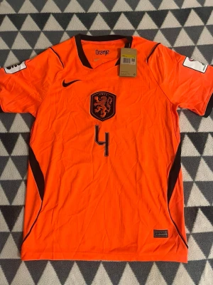 Orange fotbollströja Nike herr S - Säljer en orange fotbollströja från Nike med svarta detaljer och nummer 4 på bröstet. Tröjan har KNVB-logga och texten 'Oranje' i nacken. Perfekt för dig som älskar fotboll och vill sticka ut på planen.