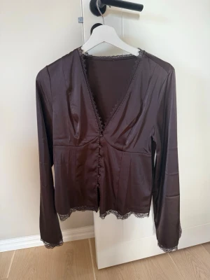 Brun satinblus med spetsdetaljer🤎 - Snygg brun blus i satin med knappar och spets. Finns ingen lapp men den är ifrån något vanligt märke som Gina,Bikbok mm. Osäker på storlek men sitter fint på mig som är en S/M🤎🌼