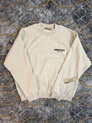 Ljusgrå sweatshirt från Essentials - Snygg ljusgrå sweatshirt från Essentials Fear of God med diskret logga på bröstet. Tröjan har rund hals, ribbade muddar och är tillverkad i mjukt bomullsmaterial. Perfekt för en clean och avslappnad stil.