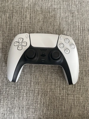 Vit och svart PS5 DualSense handkontroll - Säljer en stilren vit och svart DualSense handkontroll till PlayStation 5. Kontrollern har ergonomisk form, två analoga spakar, touchpad och klassiska PlayStation-knappar. Tillverkad i plast med matt finish och detaljer i svart. Perfekt för gaming på PS5. Kontrollen är aldrig använd