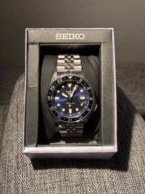 Seiko - 5 sports GMT SSK003K1 - Seiko 5 ären 3-handad automatisk klocka från Seiko som kombinerar funktionalitet och stil. Med en elegant design och robust byggkvalitet är den idealisk för både vardag och speciella tillfällen. Neon lys med lite sol, Armbandet är också i rostfritt stål. Klockan är utrustad med dag och datumvisning plus 2 olika andra tidszoner. Klarar vatten på 100 meter plus kvitto av köp på klockan finns. Storleken är 39-42 mm