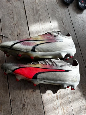 Vita fotbollsskor med röd detalj - Mycket bra puma fotbollsskor. Storlek 44. Hybrid dubbar, alltså gräs och konstgräs. Bra skick. Snygga. 