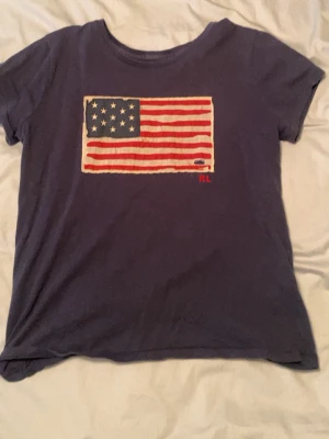 Mörkblå t-shirt med USA-flagga - Snygg mörkblå t-shirt med tryck av amerikanska flaggan på bröstet och RL-detalj i rött. Klassisk rund halsringning och korta ärmar. Perfekt för en avslappnad och cool stil.