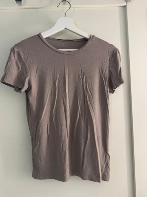 Beige basic topp i bomull - En enkel och stilren beige t-shirt med rund hals och korta ärmar. Tillverkad i mjuk bomull som känns skön mot huden. Perfekt basplagg att matcha med allt i garderoben. Storlek S från lager 157, lite nopprig men går enkelt att ta bort. Säljes då jag har för mycket kläder! 