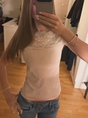 Beige topp med spetsdetalj - Säljer en beige topp med vacker spets upptill och korta ärmar. Toppen har en slim passform och är perfekt för dig som gillar feminina detaljer. Materialet känns mjukt och bekvämt mot huden. Passar till både jeans och kjol.