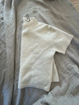 Vit stickad t-shirt med kort ärm - Snygg vit stickad t-shirt med korta ärmar och ribbade kanter. Tröjan har en högre rund halsringning och är gjord wool blend.