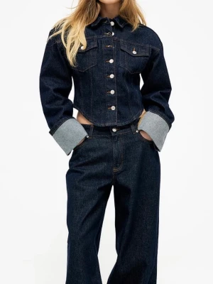 Mörkblå croppad jeansjacka - Trendig mörkblå croppad jeansjacka med markerad midja och breda uppvikta ärmslut. Klassisk krage, silverfärgade knappar och två bröstfickor med lock. Snygga kontrastsömmar ger en cool look. Perfekt för dig som vill sticka ut med en modern twist på den klassiska jeansjackan. Aldrig använd bara provad men kommer ej till användning kunde ej returna pga tog bort lappen. Den är lite i storleken så om du har S skulle denna passa för dig