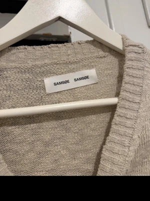 Beige stickad tröja Samsøe Samsøe - Snygg beige stickad tröja från Samsøe Samsøe. Tröjan har rund halsringning, ribbade muddar och är tillverkad i ett mjukt, tunt stickat material. Perfekt för lager på lager och enkel att matcha med olika outfits.