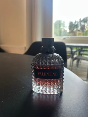 Valentino parfym med nitat glasflaska - Snygg parfym från Valentino i en genomskinlig glasflaska med nitat mönster och svart etikett. Vätskan är rosaröd och flaskan har en svart kork med detaljer. Perfekt för dig som gillar lyxiga och stilrena dofter. Ungefär 80ml kvar i flaskan. Skickas i orginalförpackning.