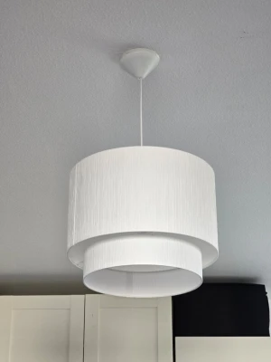 Vit taklampa från H&M - Säljer en modern vit taklampa med två cylinderformade lampskärmar i olika storlekar. Lampan har en stilren och enkel design som passar bra i de flesta rum. Köpt juli 2025, jättefin fräsch o elegant lampa 