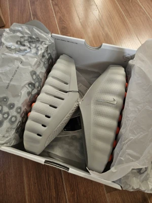 Nike Mind 001 tofflor med orange sula - Tänk om du kunde lyfta din matchförberedelse med en sko som förändrar känslan helt? Vi presenterar Nike Mind. De stora yttersulesektionerna trycker mot foten när du går och stimulerar hjärnans sinnesområden för att hjälpa dig att vara närvarande och känna kontakten med omgivningen. När allt står på spel är det ditt mindset som avgör segern.