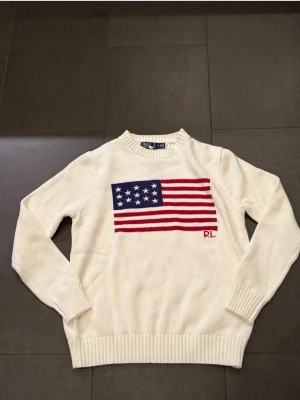 Ralph lauren flag sweater  - Ralph lauren stickad tröja med amerikansk-flagga på framsidan. Helt ny-skick, säljs då den inte passar! Storlek L men har krympt. Skriv vid funderingar! 