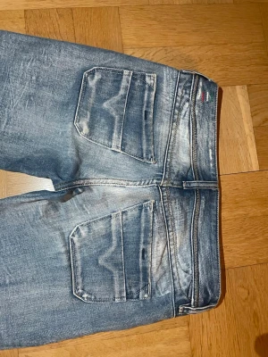 Diesel jeans raka med slitningar - Ljusblå jeans med raka ben, slitna detaljer och fransade benslut. Jeansen har klassiska bakfickor med diskret mönster och en liten detalj i rött och vitt vid linningen. Perfekta för en avslappnad och trendig look. Tyvärr för korta för mig som är 162cm🥰. (Jeansen är väldigt stela i knäna)