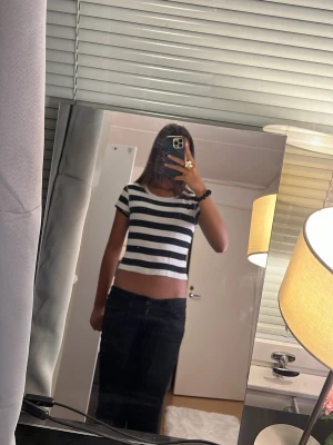 Randig svartvit t-shirt från Lindex - Säljer en kortärmad och kroppad t-shirt från Lindex i svart och vitt med breda horisontella ränder. T-shirten har en klassisk rund halsringning och är gjord i mjuk bomull. Ser kort ut på bilden men är för att den är för liten