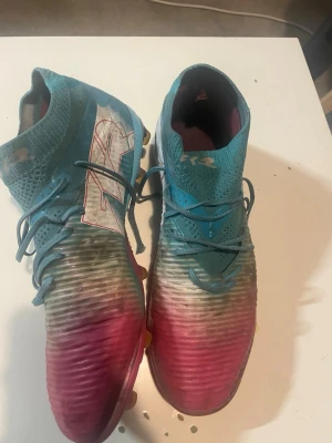 Blå och rosa fotbollsskor med snörning - Säljer ett par snygga fotbollsskor i blått och rosa med högt skaft och snörning. Skorna har en ribbad ovansida för bättre bollkontroll och en färgglad sula med dobbar för spel på gräs. Materialet är en mix av syntet och textil för bra komfort och passform. Priset kan diskuteras, priset kan man tycka är för högt, men dessa skor är ultimate, men jag tar emot bud.! 