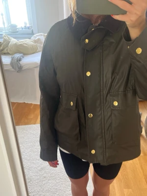 Mörkgrön jacka med guldknappar - Snygg mörkgrön jacka i oversized modell med stora fickor och guldiga knappar framtill. Jackan har hög krage och är perfekt för lager på lager. Passar dig som gillar en avslappnad och trendig stil.