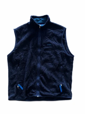 Vintage Patagonia Synchilla Fleece Vest – L - Vintage Patagonia Synchilla fleeceväst i mörkblå/navy, storlek L. Äldre Made in USA-modell med full zip, två dragkedjeförsedda fickor och klassisk Patagonia-logga på bröstet. Snygg vintage outdoor/gorpcore-look och en betydligt mer intressant modell än moderna standardfleece. Fint begagnat skick enligt bilder (lätt hårig och nopprig). Mått skickas gärna. Bud välkomnas & snabb frakt 📦