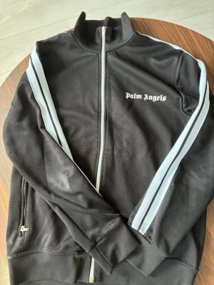  Palm angels tröja  - Säljer denna feta Palm angels tröjan för den blivit för liten. Tröjan är i strlk M. Den är i mycket bra skick. De ända är att dragkedjan kan bli lite konstig men enkelt att fixa. Som man kan se på bilden är den lite smutsig på ärmen men tvättar den och fixar den innan den fraktas. Vid frågor skriv! 