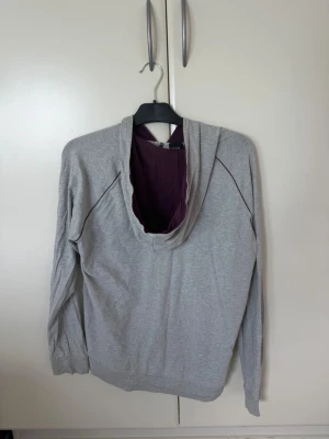 Grå hoodie från BOSS med dragkedja - Snygg grå hoodie från BOSS med dragkedja framtill och svart BOSS-logga på bröstet. Hoodien har långa ärmar, fickor på sidorna och en huva med lila innerfoder. Tillverkad i mjukt och bekvämt material, perfekt för en avslappnad stil.  Kan mötas upp om de är nära halmstad/göteborg