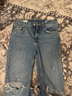 Jeans från Zara  - Säljer ett par blå jeans med raka ben med hål på knänen, dem är lite slitna längst ner på baksidan!! 